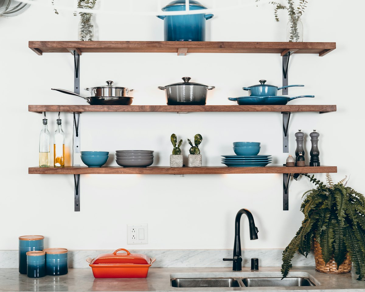 Open kitchen shelves holding jars, pots, and dishes above a sink